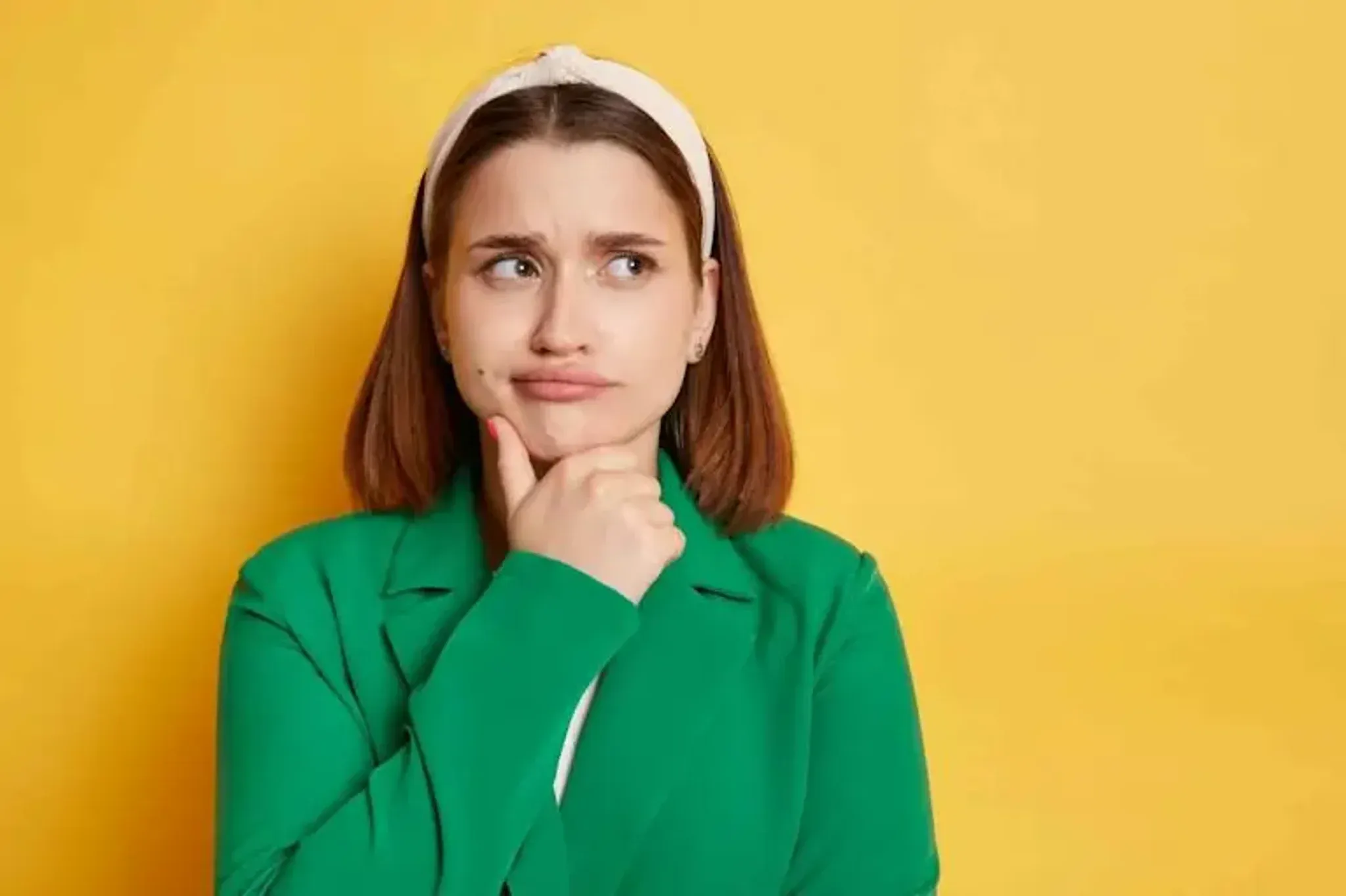 Woman looking thoughtful with her hand on her chin against a yellow background.